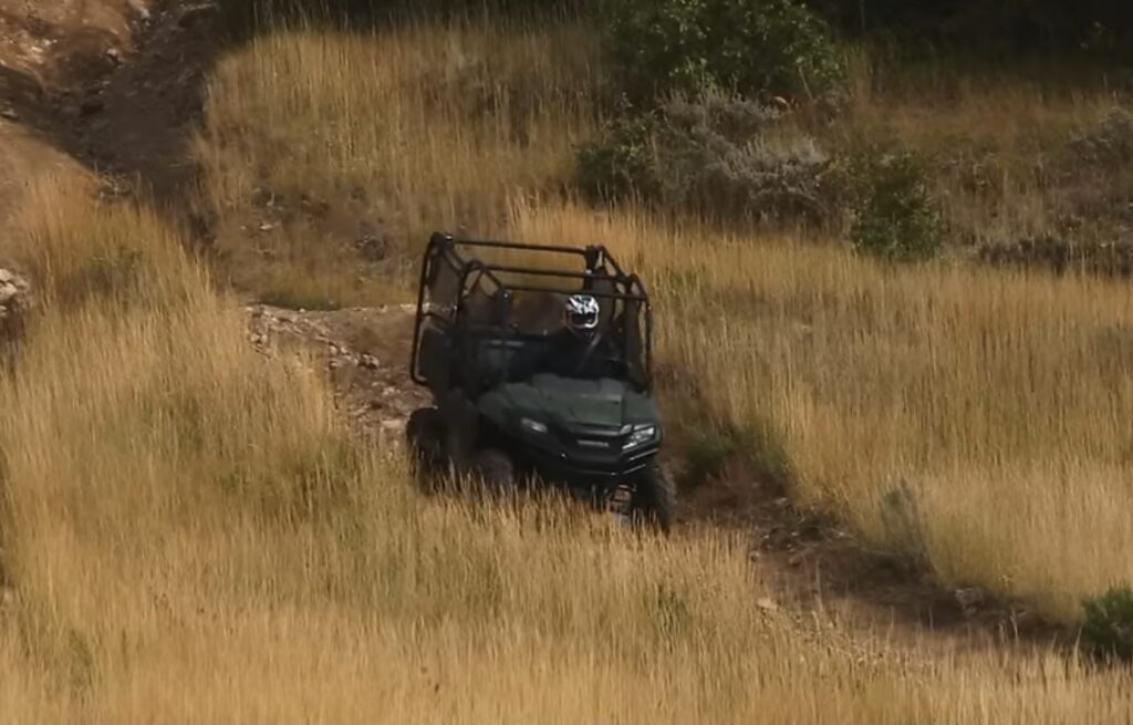 A Honda Pioneer 700 is being driven through a grass field.