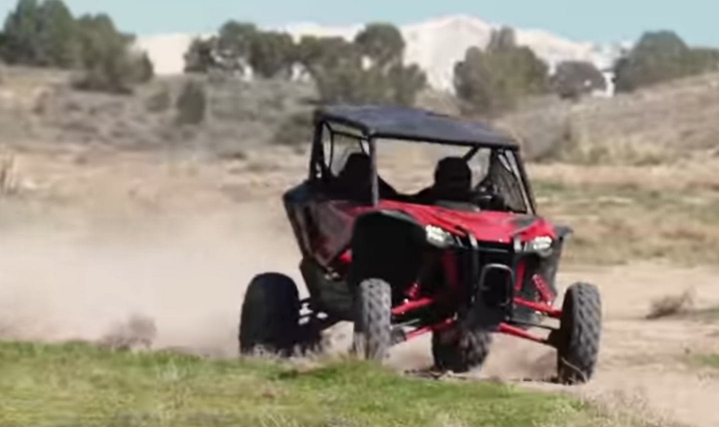 A Honda Talon 1000 is being driven through a dirt and dusty road.