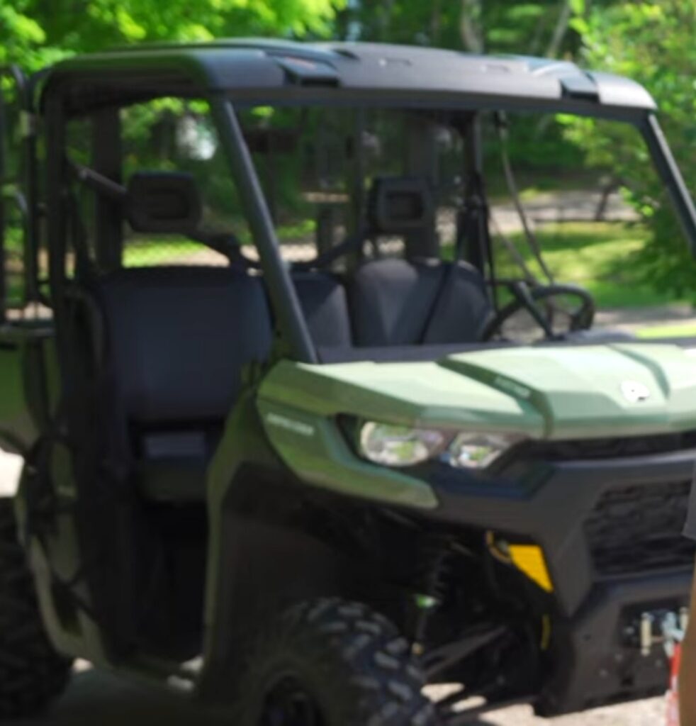 A Can-Am defender is parked under some trees.