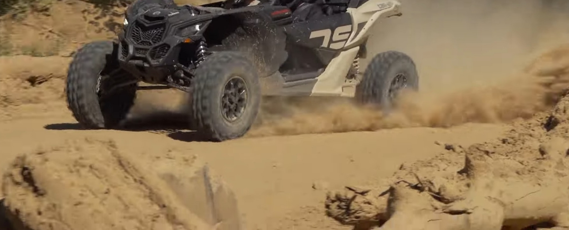 A Can-Am Maverick X3 is being driven through a dirt and dusty trail.