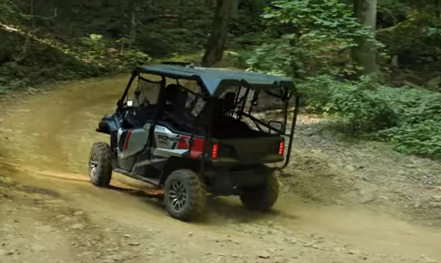 A Honda Pioneer 1000 is being driven through a dirt road in a jungle.