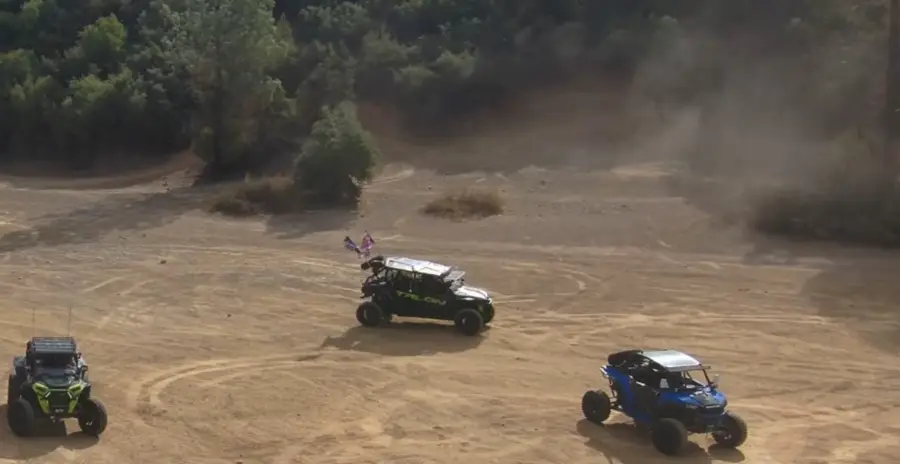 Three Polaris UTVs parked on a dirt surface 
