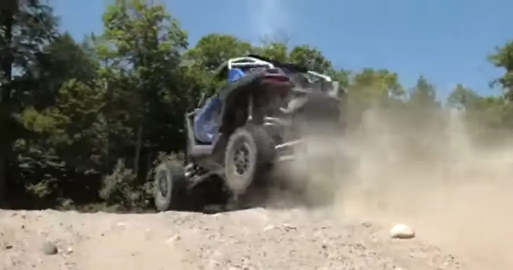 A Polaris RZR UTV is being driven through a gravel road.