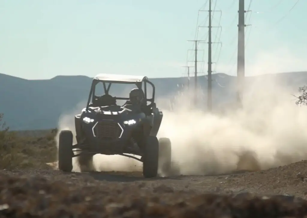 A Polaris RZR XP Turbo S is being driven through a dirt and dusty road.