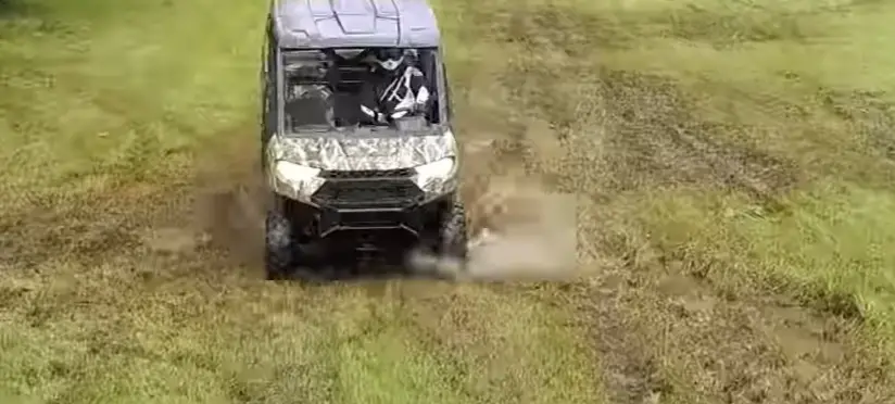 A Polaris Ranger 1000 is being driven through a muddy road.