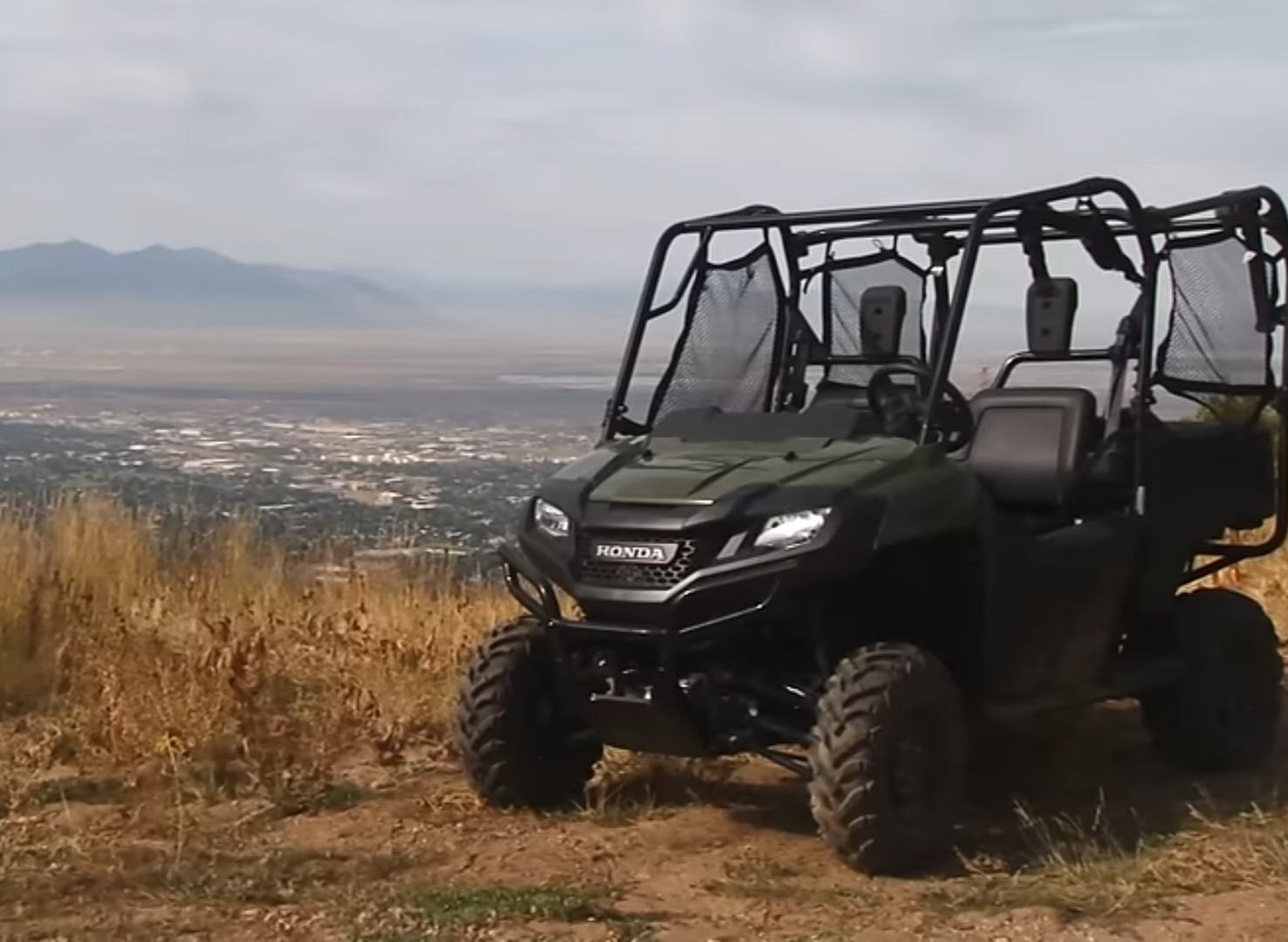 A Honda Pioneer 700 is parked on the top of a hill. In the background there are mountains and beautiful blue sky.