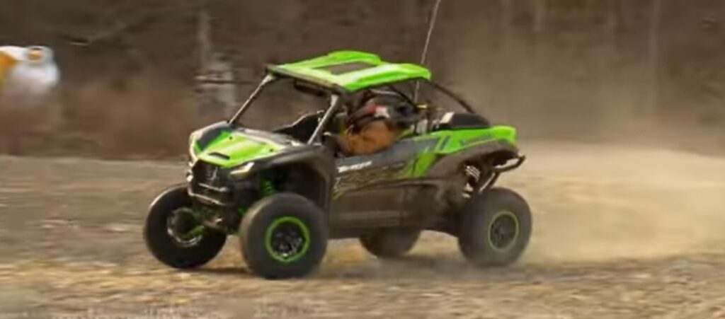 A Kawasaki teryx UTV is being driven through a dirt road.