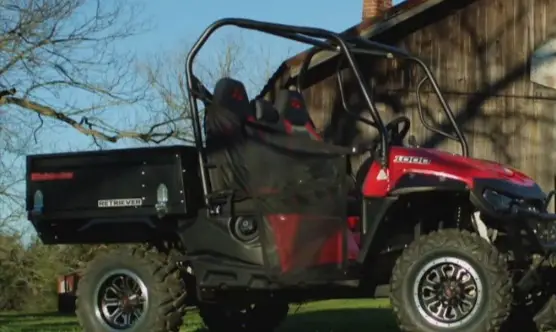 A Mahindra Retriever is parked in front of a farmhouse.