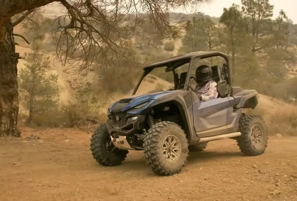 A Yamaha Wolverine RMAX2 is being driven through a dirt road.