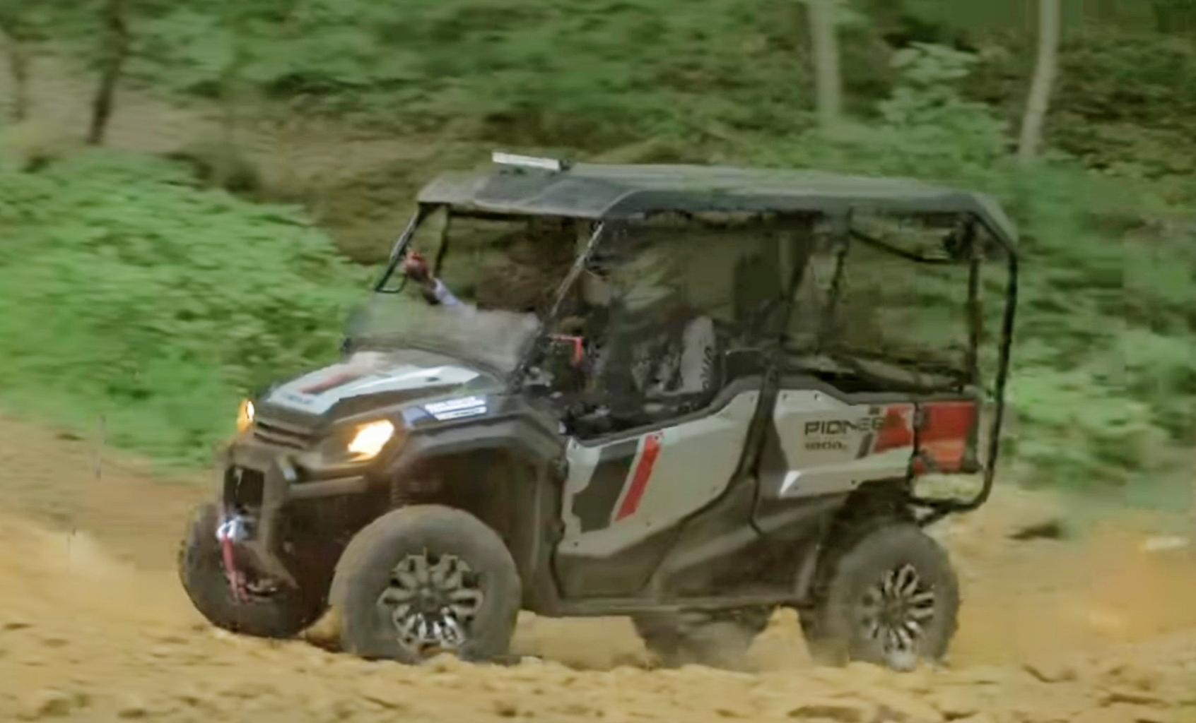 A Honda Pioneer 1000 is being driven through a jungle terrain.