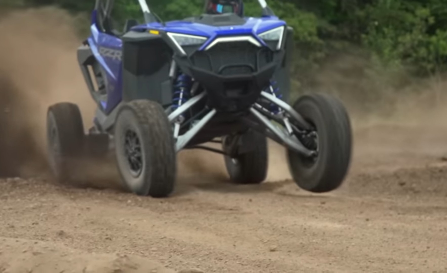 A Polaris RZR is being driven through a dirt and dusty road.