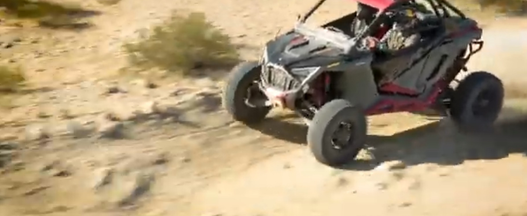 A Polaris RZR UTV is being driven through a dirt and gravel road.