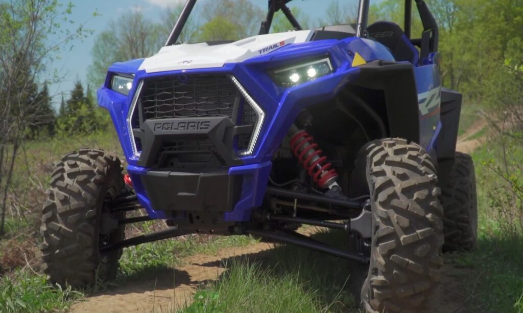 A Polaris RZR 1000 is parked on a dirt grass surface.