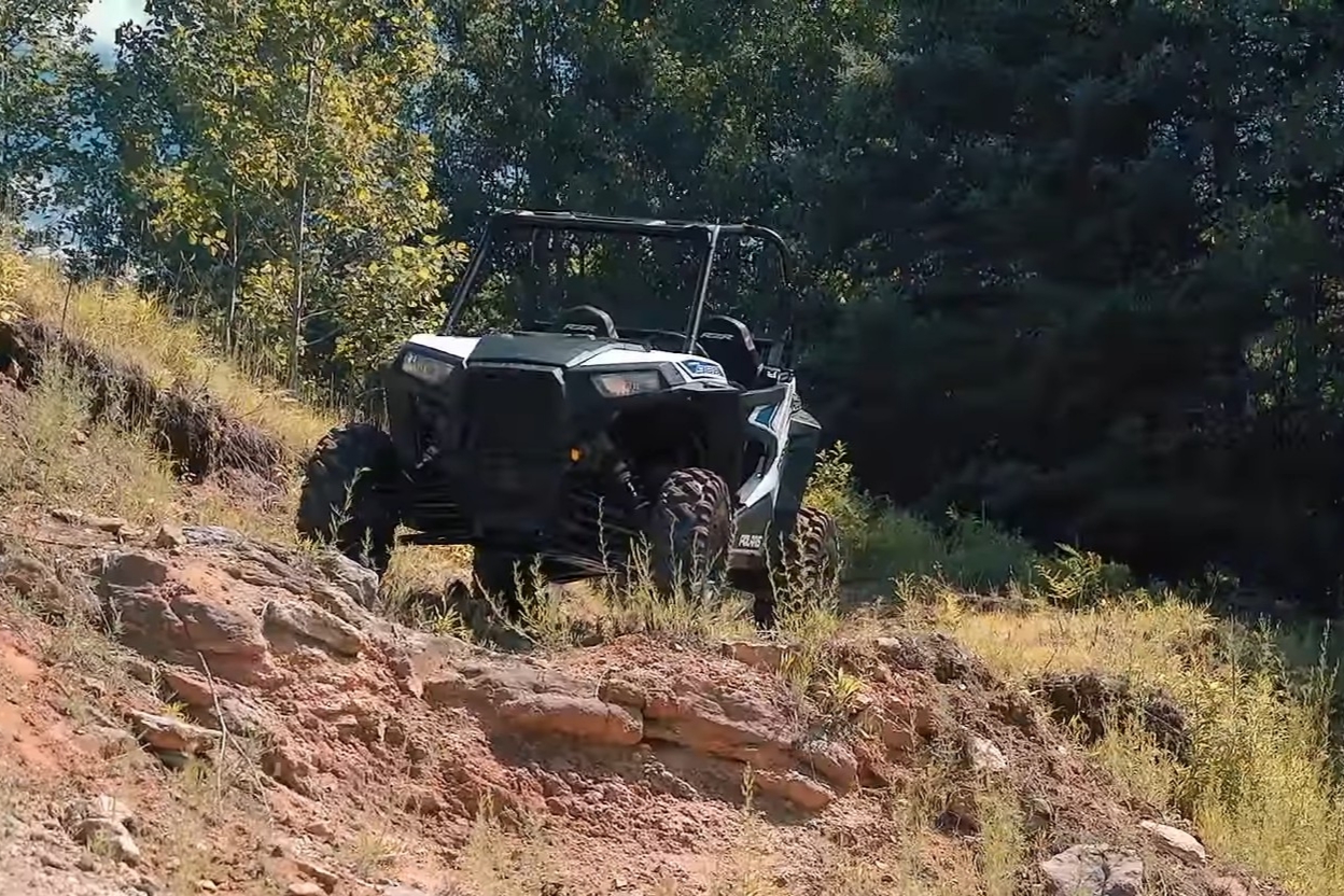 A Polaris RZR 900 is parked in front of a forest.