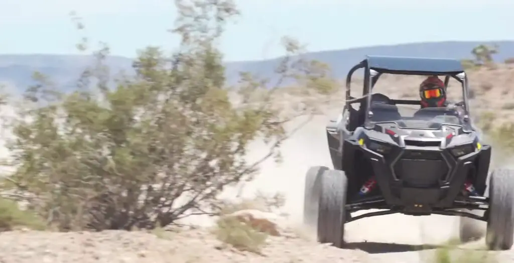 A Polaris RZR Turbo S is being driven through a dirt and dusty road.