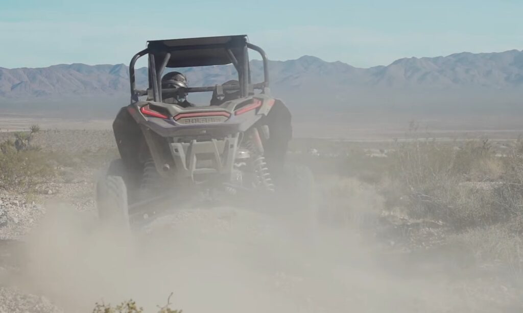 A Polaris RZR XP Turbo S is being driven through a dusty trail.