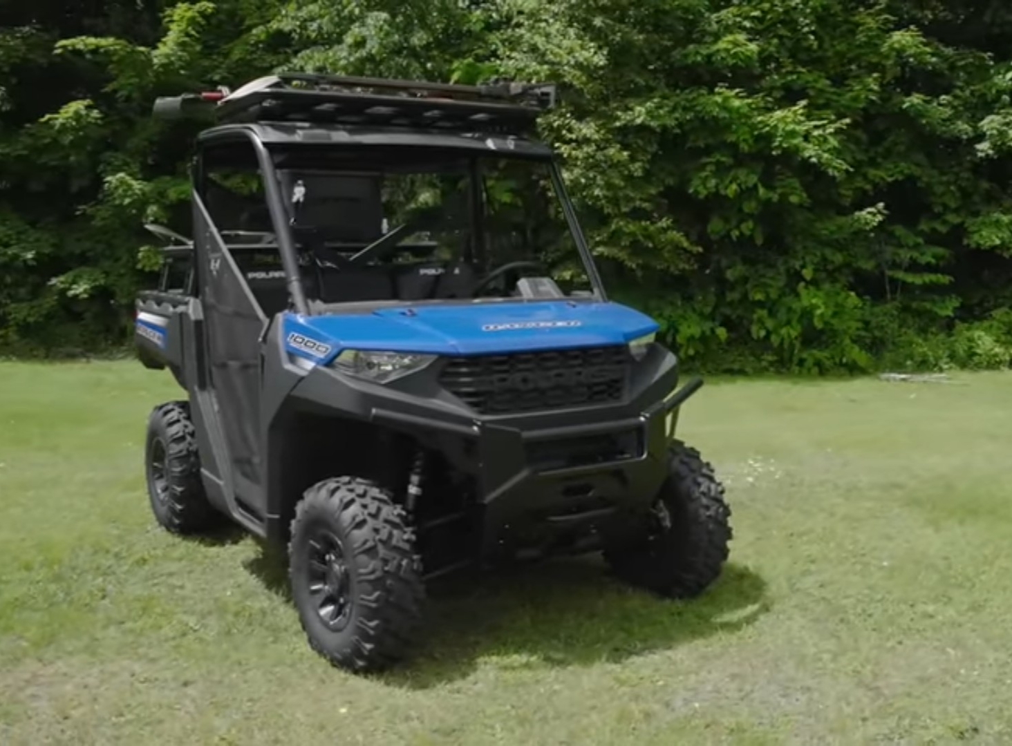 A Polaris Ranger 1000-Polaris Diesel UTV is parked in a green field. In the background there are trees and bushes.