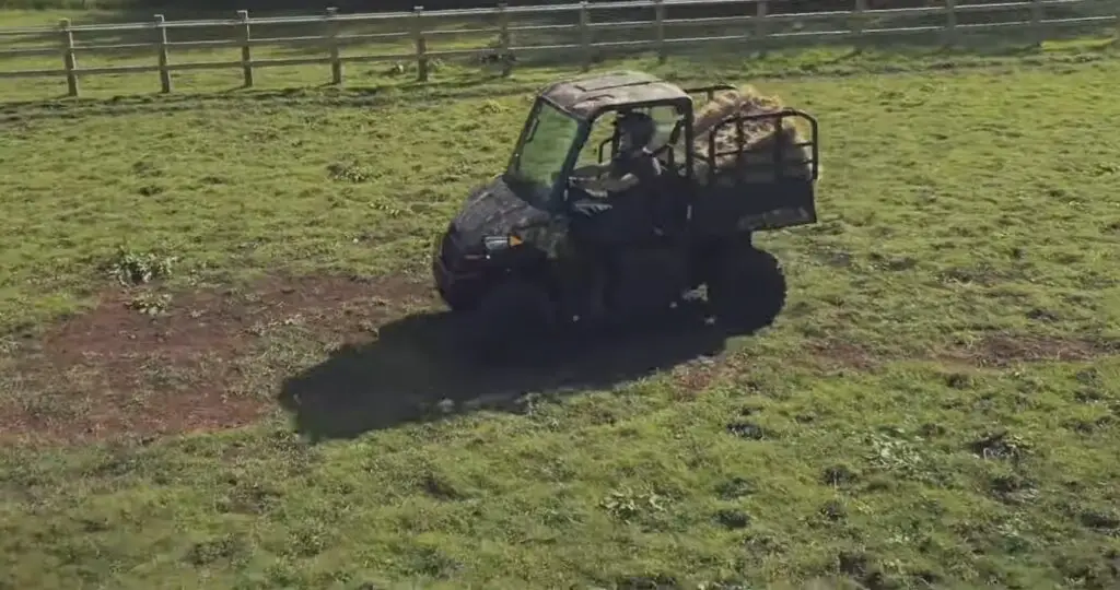 A Polaris Ranger EV with loaded dump bed is being driven through a green field with fence.