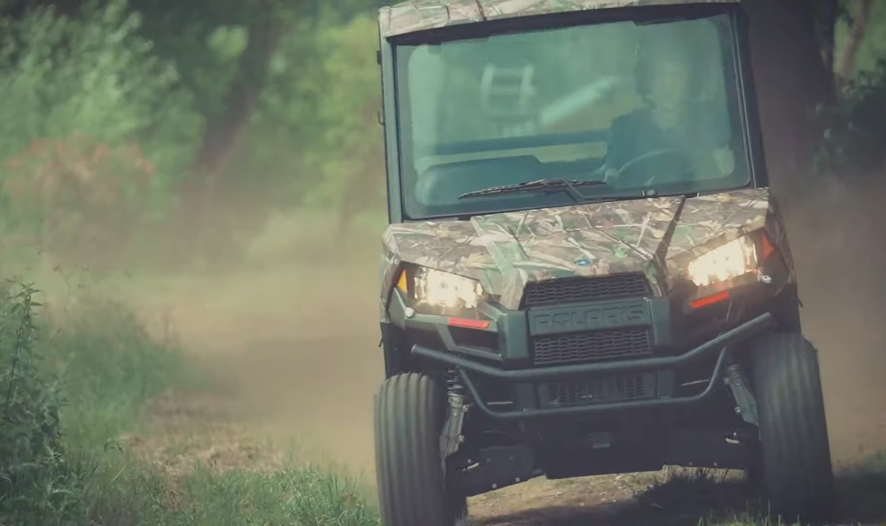 A Polaris Ranger EV is being driven through a dirt and dusty road.