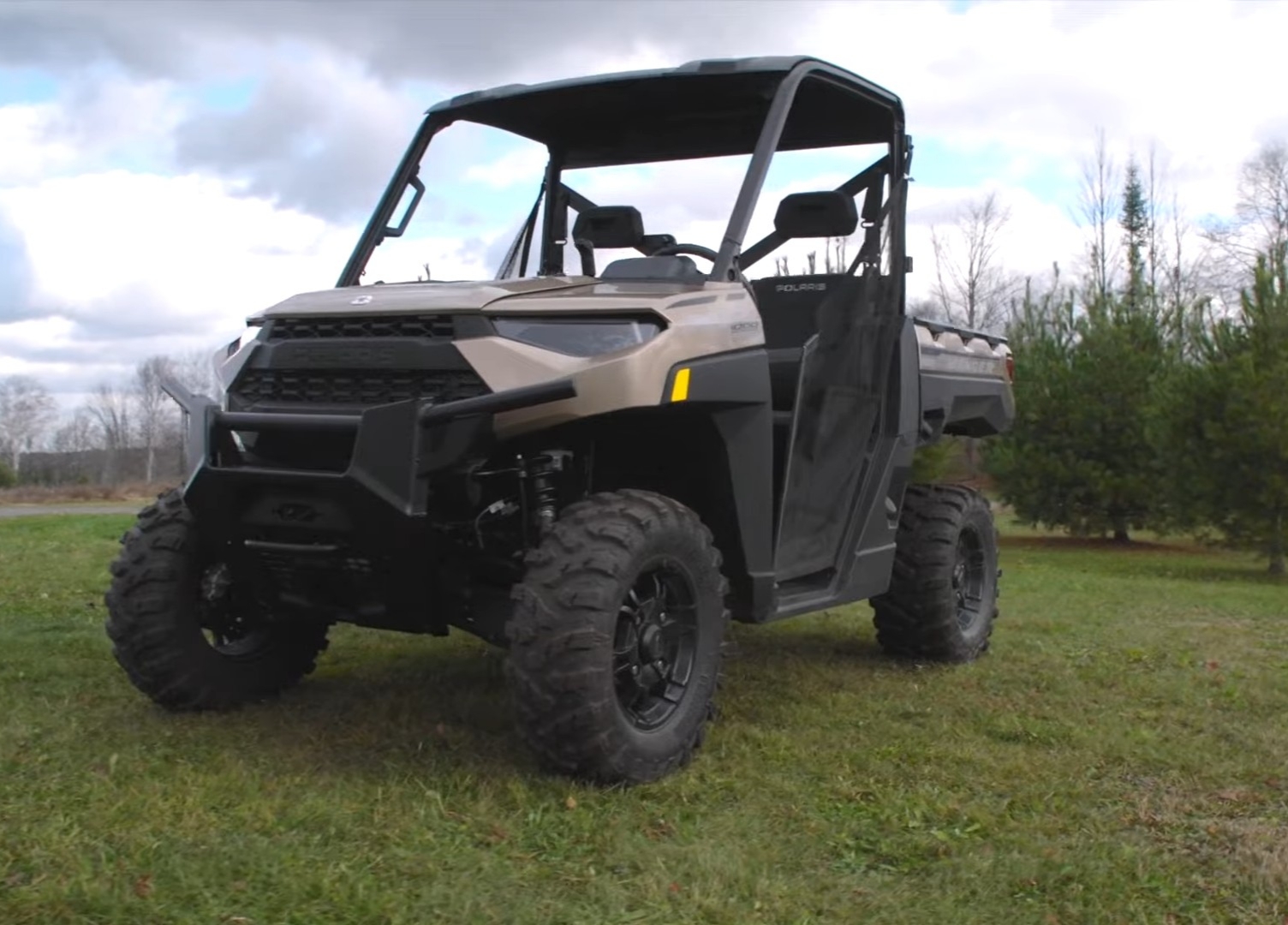 A Polaris Ranger XP 1000 is parked in a green field. In the background there is white sky with clouds.