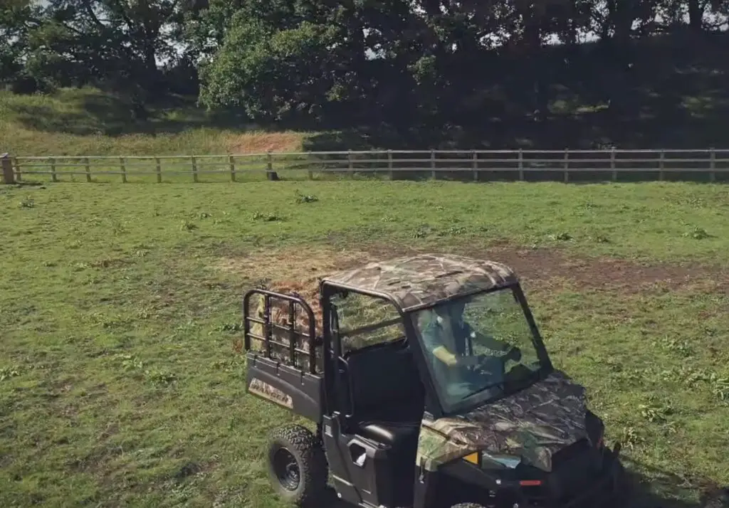 A Polaris Ranger EV with loaded dump bed is being driven through a green field.