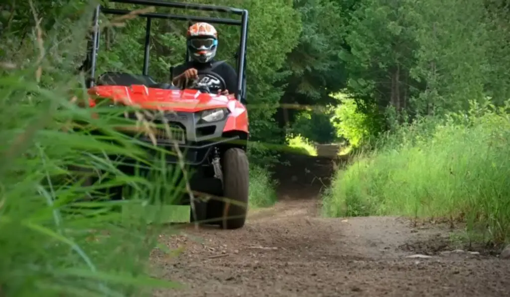 A Polaris Ranger 500 is being driven through a dirt road. There are trees and bushes on the both side of the road.