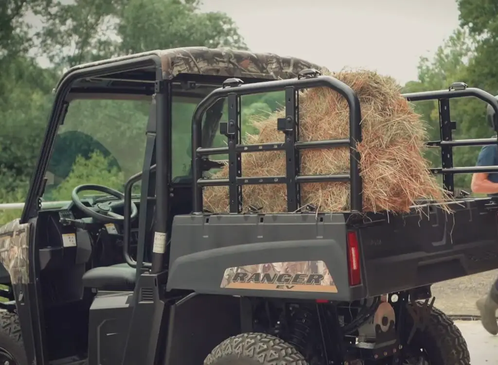 A Polaris Ranger EV with loaded dump bed is parked in front of a farm house.