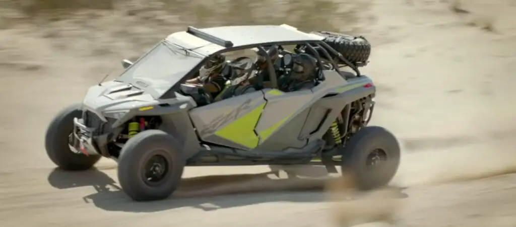 A Polaris RZR is being driven through a dirt road.