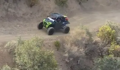 A Polaris UTV is being driven through a dirt and dusty road.