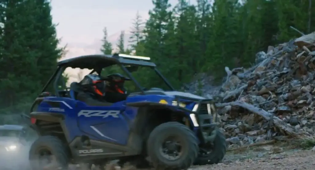 A Polaris RZR is being driven through a jungle terrain.