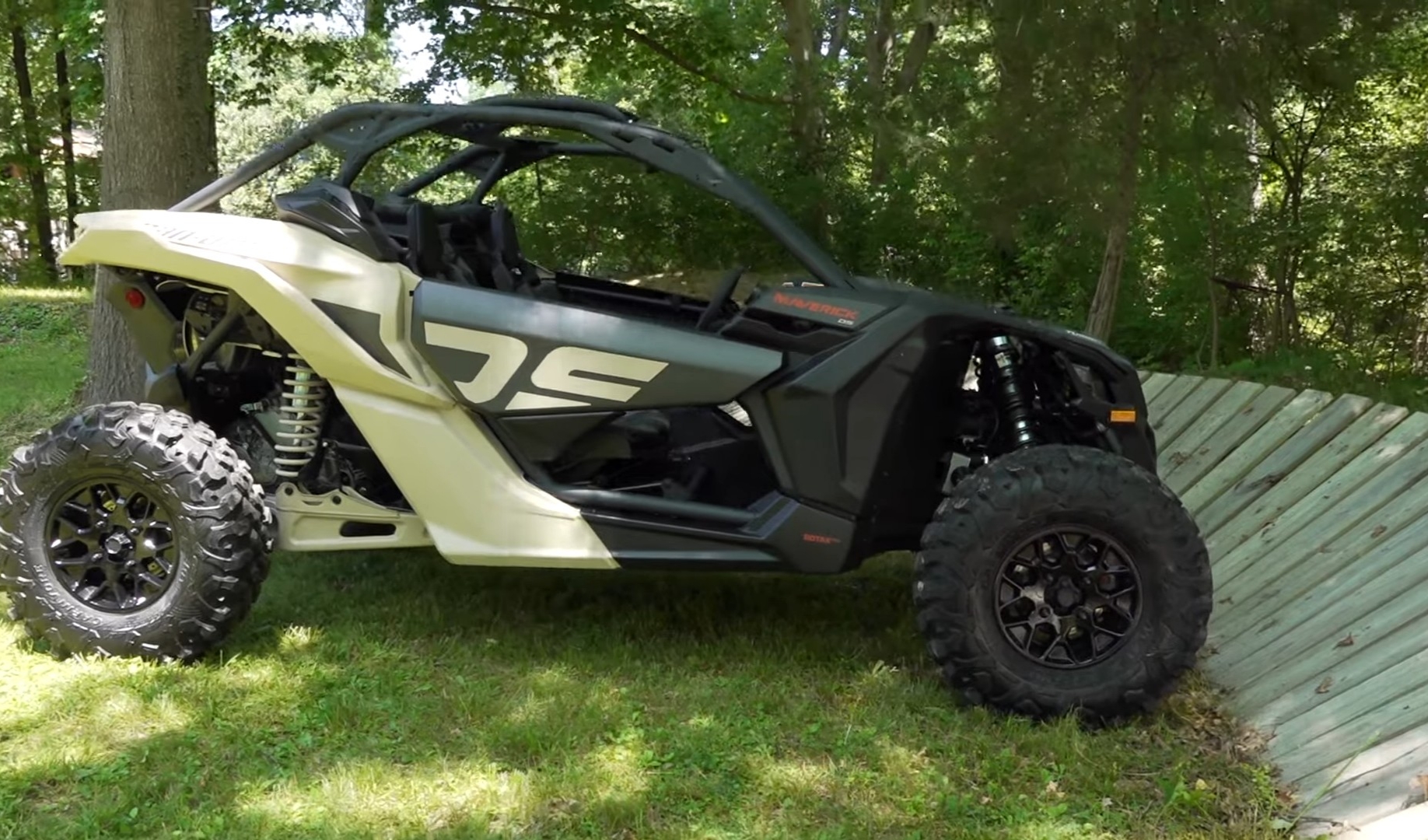 A Can-Am Maverick X3 is parked on a grassy field under some trees.