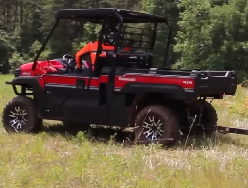 A Kawasaki Mule Pro FX LE is parked in a green field in front of a forest.