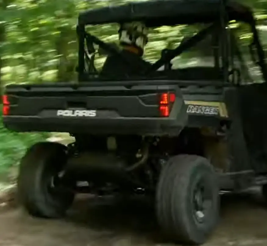 A Polaris Ranger 1000 is being driven through a forest road.