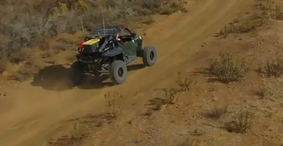 A Polaris UTV is being driven through a dirt and dusty road.