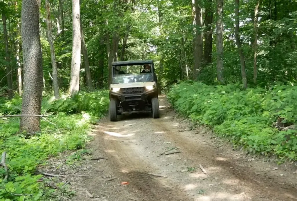 A Polaris Ranger is being driven through a jungle road.