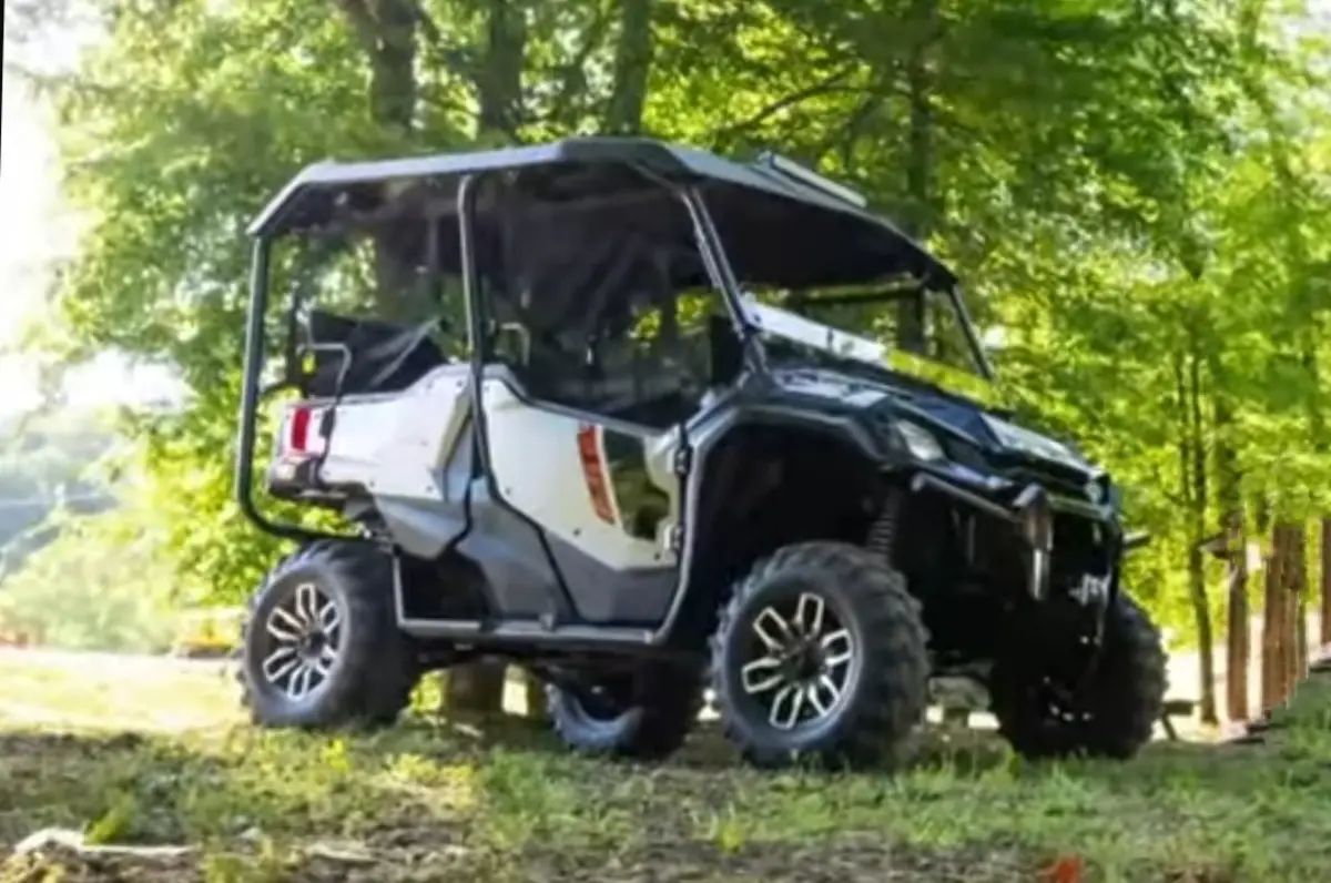 A Honda Pioneer 1000 is parked under some trees.