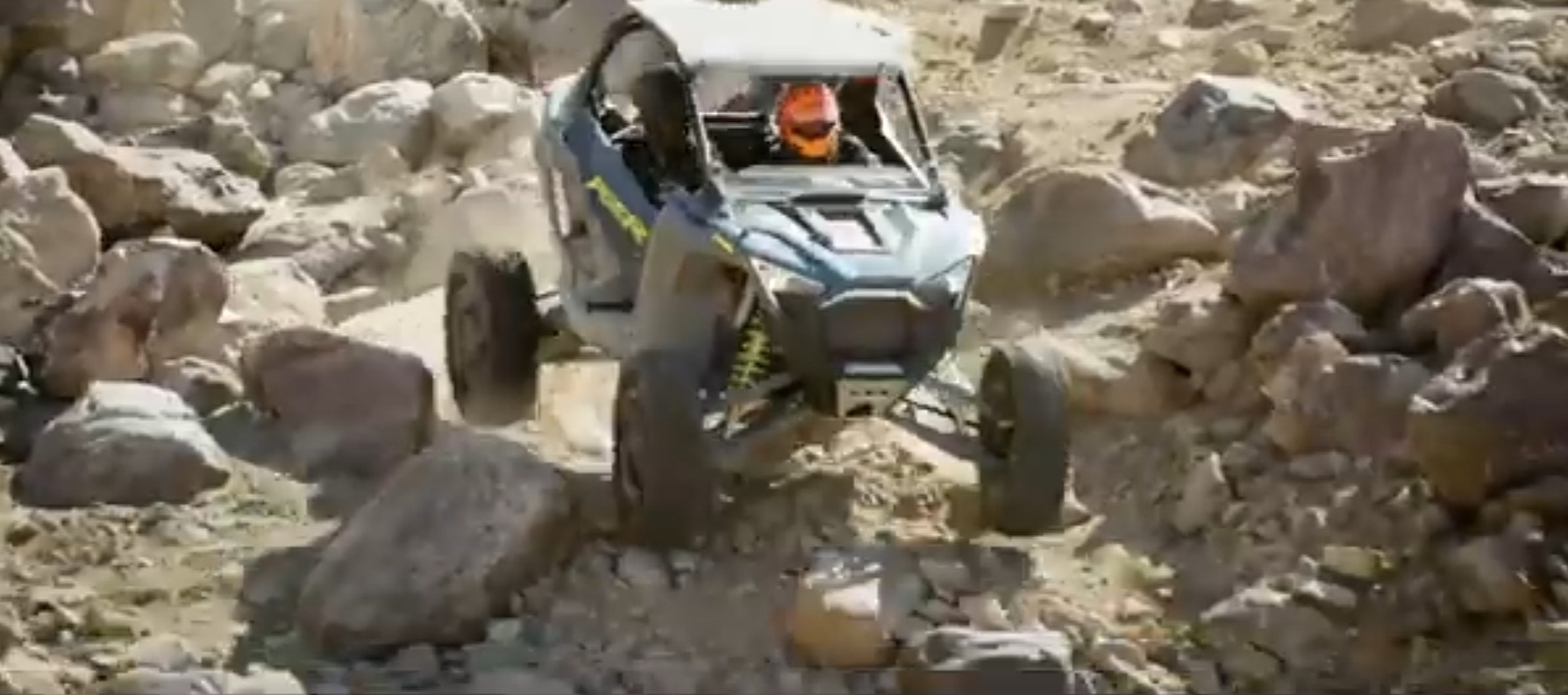 A Polaris UTV is being driven through a gravel road.