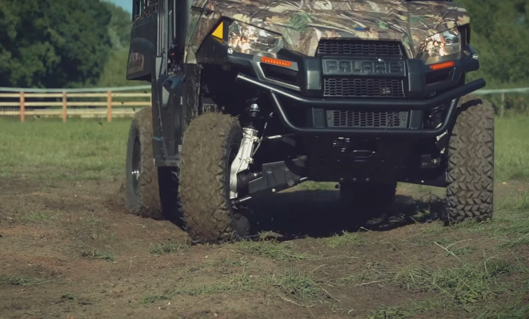 A camo Polaris Ranger EV is parked on a dirt and grassy field.