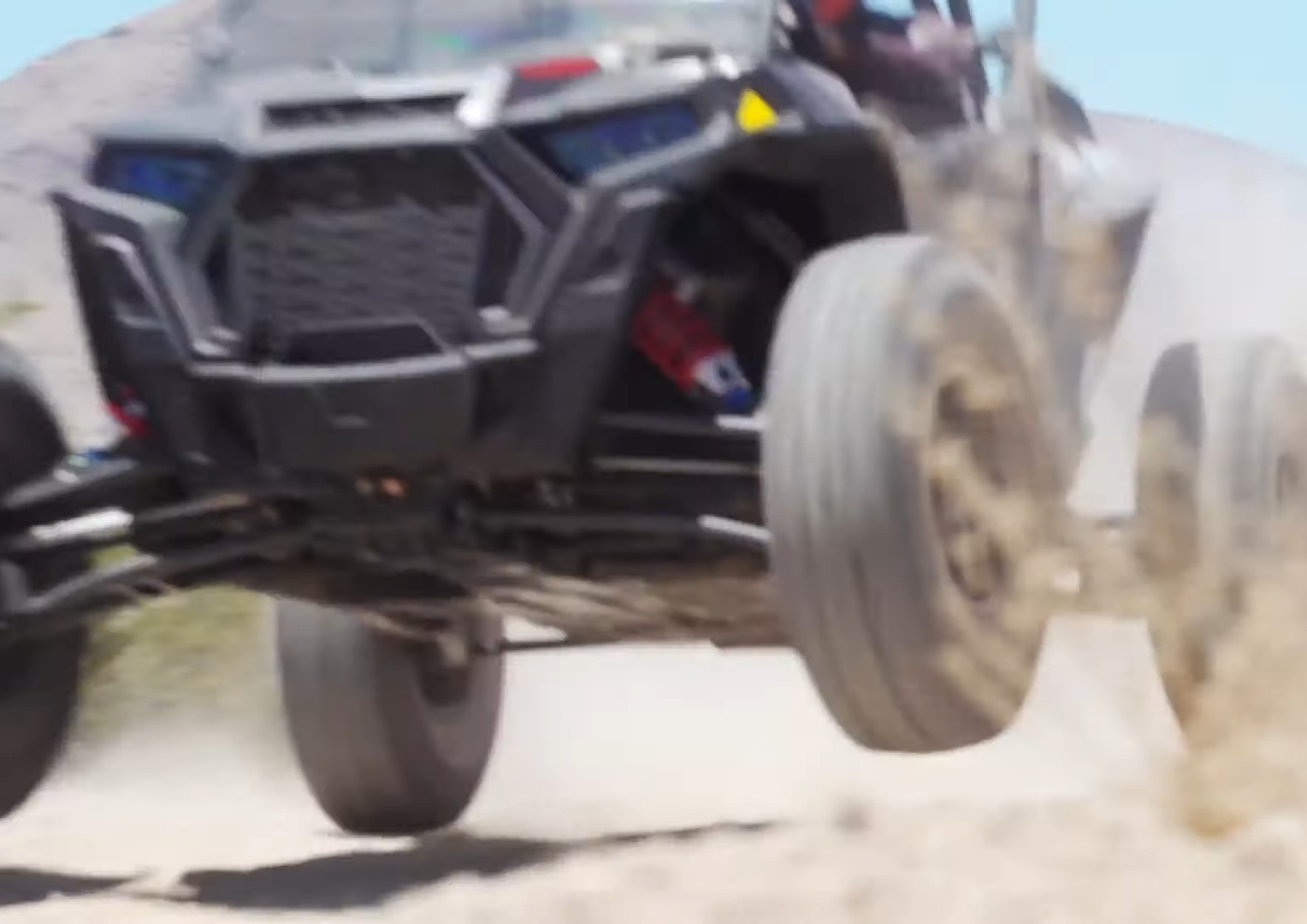 A Polaris RZR Turbo S is being driven through a desert sand road.