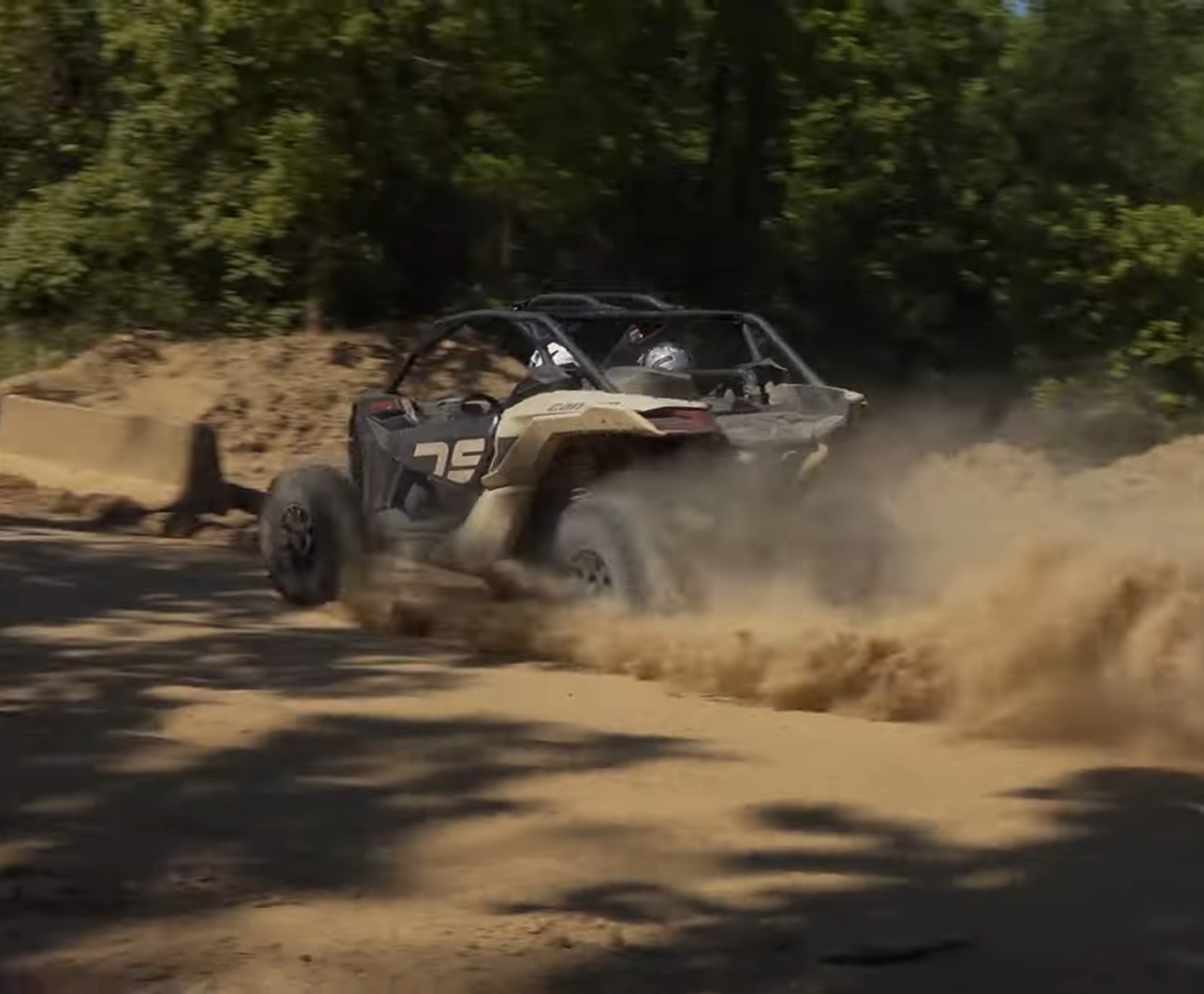 A Can-Am Maverick X3 is being driven through a dusty trail.