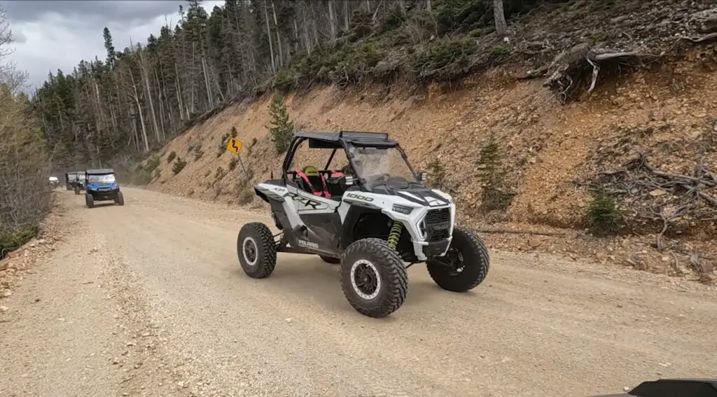 A Polaris RZR is being driven through a hill road.