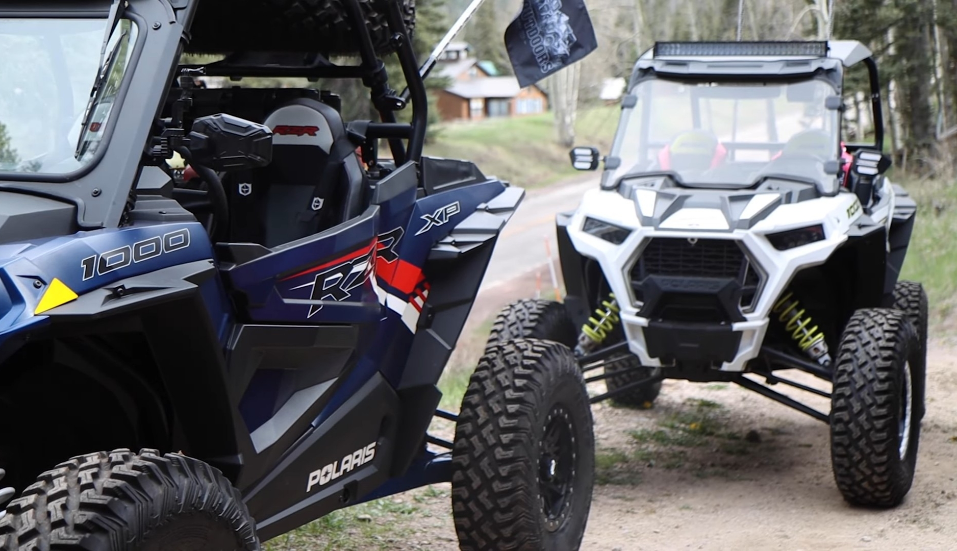 Two Polaris RZR UTVs are parked on a dirt road.