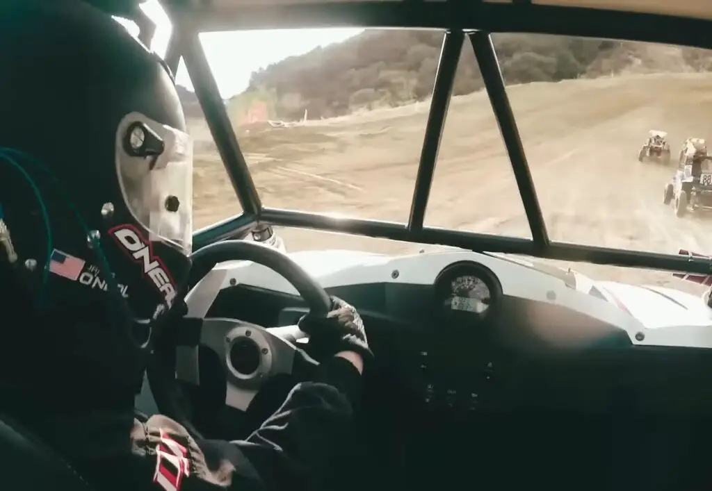 A UTV is being driven by a child through a dirt road.