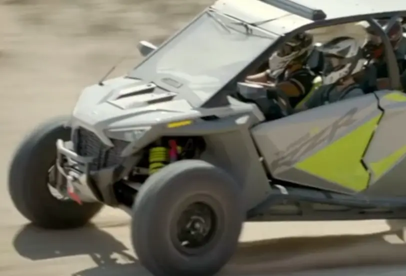 A Polaris RZR is being driven through a dirt road.