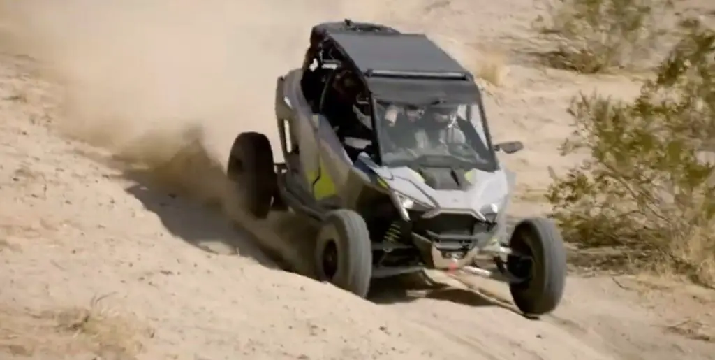 A Polaris RZR is being driven through a desert road.