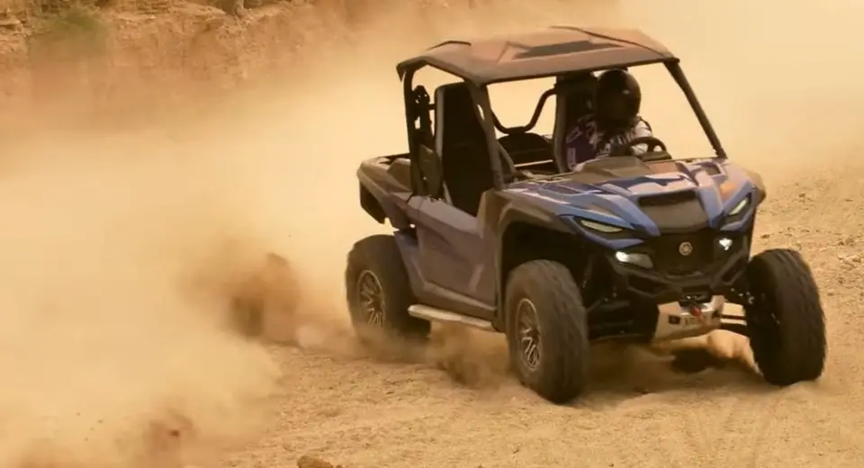 A Yamaha RMAX2 is being driven through a dirt and dusty desert road.