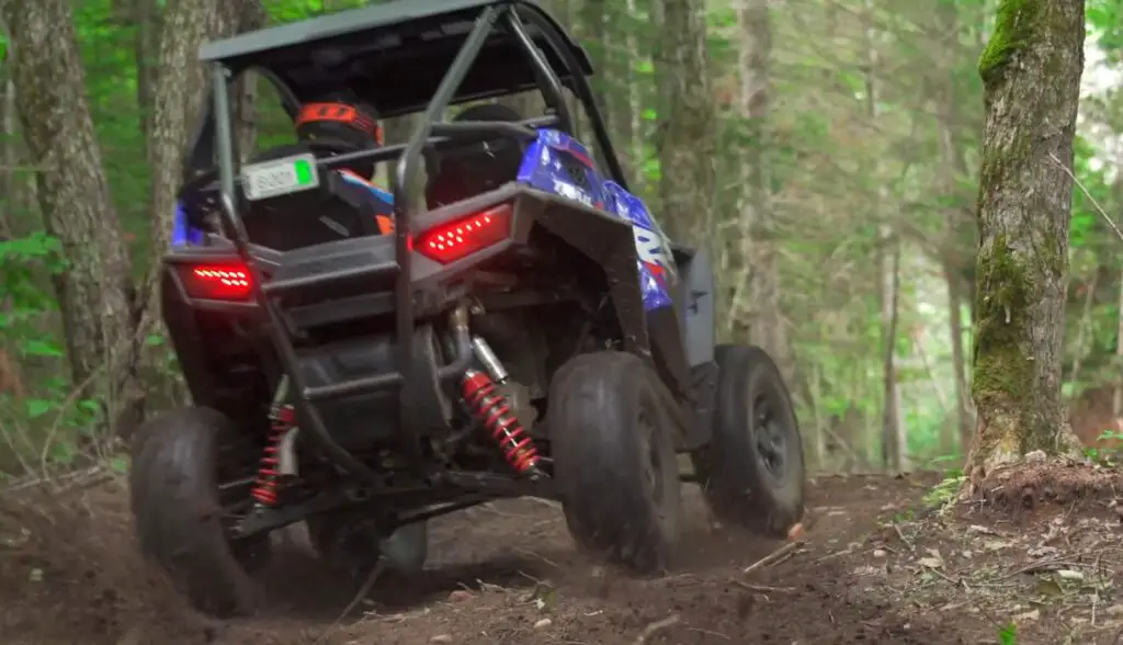 A Polaris RZR is being driven through a dirt jungle terrain.