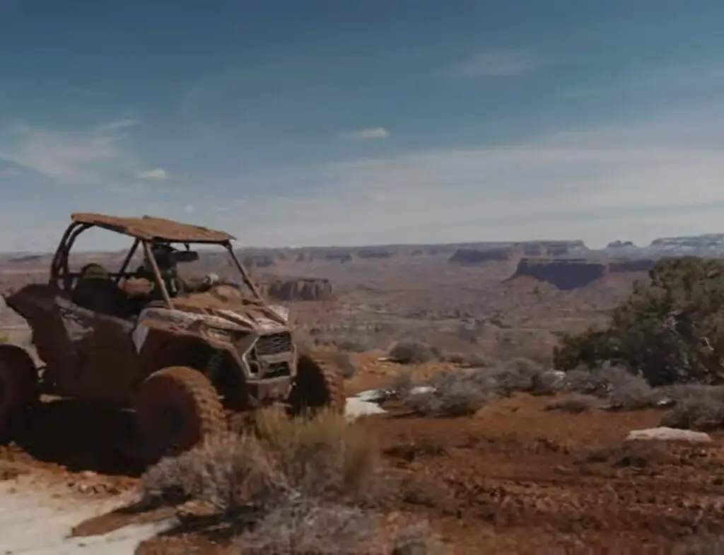 Polaris RZR 1000 is being driven through a dirt road.