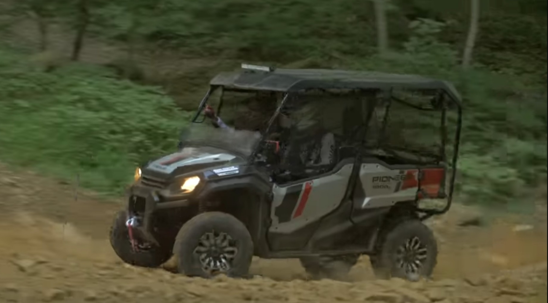 A Honda Pioneer 1000 is being driven through a dirt road.