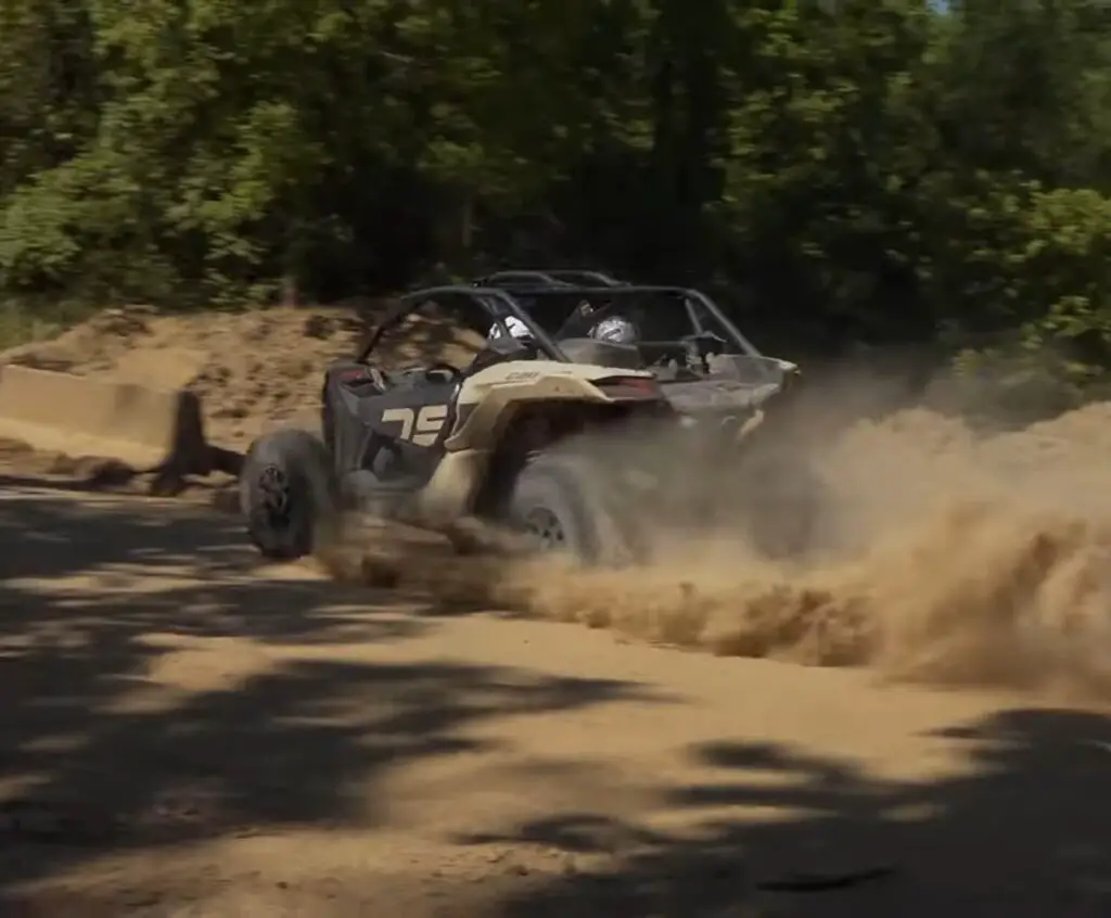 A Can-am Maverick X3 is being driven through a dirt and dusty trail.